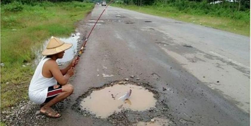 A man pretends to fish out of a pothole in a section of the Mawlamyine-Thanbyuzayat road. (Photo – Facebook)