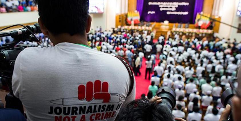 သြဂုတ် ၂၈၊ ၂၀၁၈ ခုနှစ်က ပြုလုပ်ခဲ့သည့် အခမ်းအနားတစ်ခုဖြစ်သော နိုင်ငံတော်အတိုင်ပင်ခံ ဒေါ်အောင်ဆန်းစုကြည်က ရန်ကုန်တက္ကသိုလ်ကျောင်းသားများကို မိန့်ခွန်းပြောကြားခိုက် " ဂျာနယ်လစ်ဇင်သည် ရာဇဝတ်မှု မဟုတ်ပါ" ဆိုသော ကြွေးကျော်သံပါ တီရှပ်တထည်ဝတ်ဆင်ထားသော သတင်းသမားတစ်ယောက်ကို တွေ့ရစဉ်။ ဓာတ်ပုံ- အေအက်ဖ်ပီ