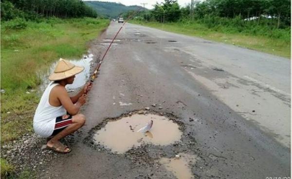 A man pretends to fish out of a pothole in a section of the Mawlamyine-Thanbyuzayat road. (Photo – Facebook)
