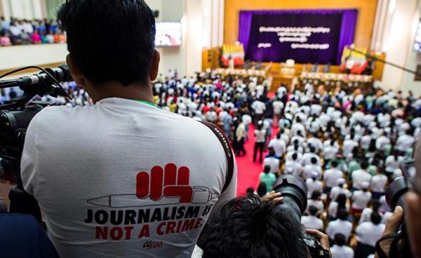 သြဂုတ် ၂၈၊ ၂၀၁၈ ခုနှစ်က ပြုလုပ်ခဲ့သည့် အခမ်းအနားတစ်ခုဖြစ်သော နိုင်ငံတော်အတိုင်ပင်ခံ ဒေါ်အောင်ဆန်းစုကြည်က ရန်ကုန်တက္ကသိုလ်ကျောင်းသားများကို မိန့်ခွန်းပြောကြားခိုက် " ဂျာနယ်လစ်ဇင်သည် ရာဇဝတ်မှု မဟုတ်ပါ" ဆိုသော ကြွေးကျော်သံပါ တီရှပ်တထည်ဝတ်ဆင်ထားသော သတင်းသမားတစ်ယောက်ကို တွေ့ရစဉ်။ ဓာတ်ပုံ- အေအက်ဖ်ပီ