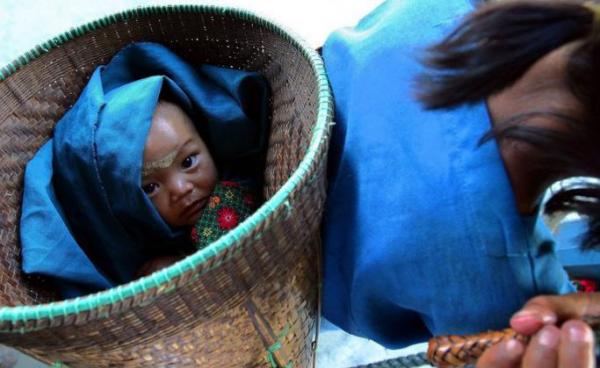 A tribal baby is carried in a basket as her parents head to pick up their rice and yuan payment after labouring in the fields, in north-eastern Myanmar. Photo: EPA