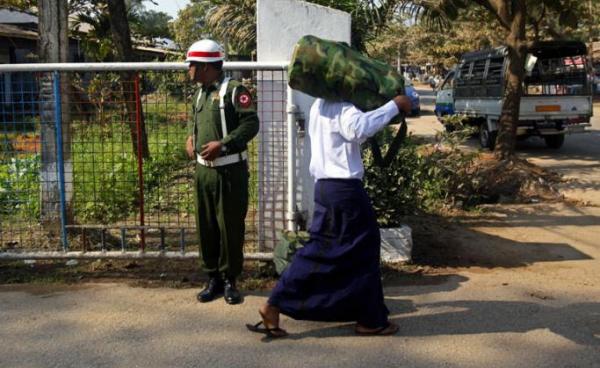 (File) Myanmar boy wearing a white shirt (R), who was discharged from Myanmar army, loads a bag on his shoulder as he walks near a military man at a gate of military compound - 18 January 2014. Photo: Lynn Bo Bo/EPA